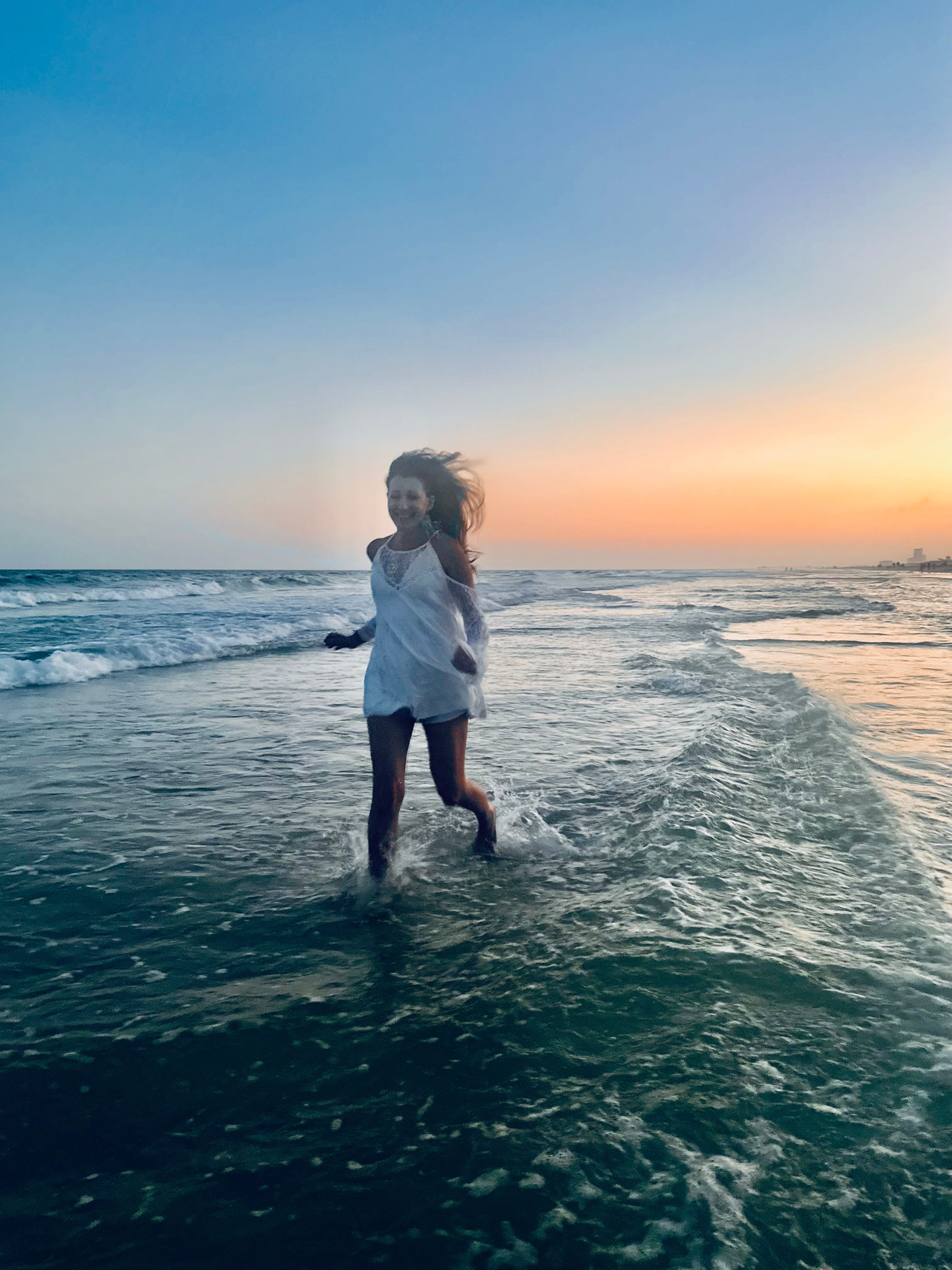 Person standing in the ocean at sunset with a colorful sky.
